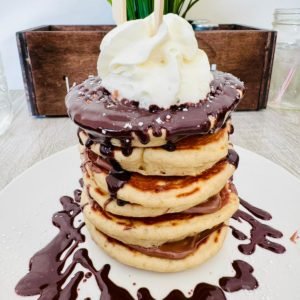 stacked pancakes with chocolate and whipped cream